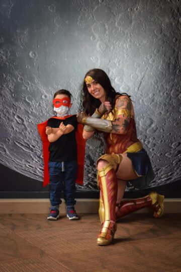 Wonder Woman posing with a young child posing with a red eye mask. 