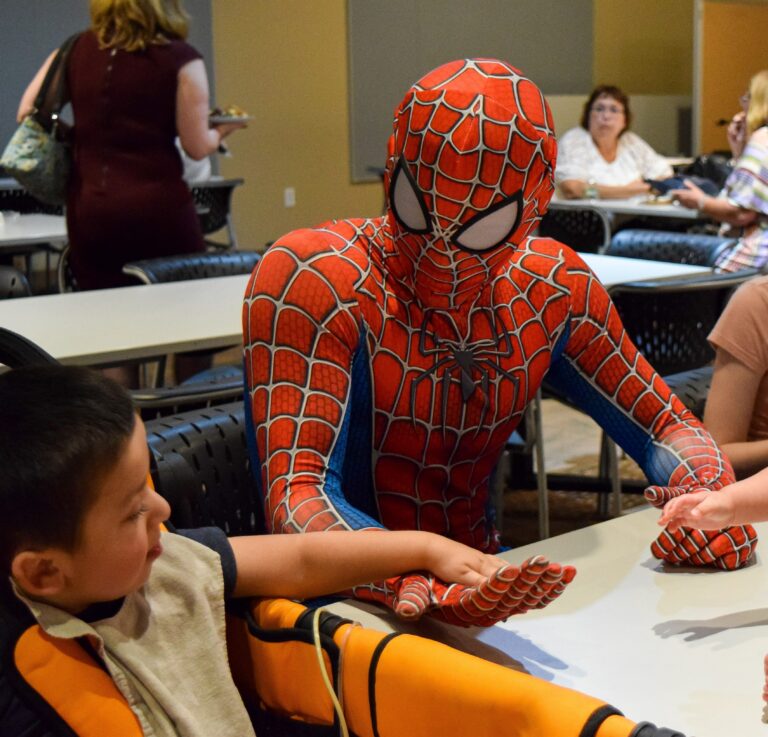 Spiderman sitting at a table holding the hand of a child
